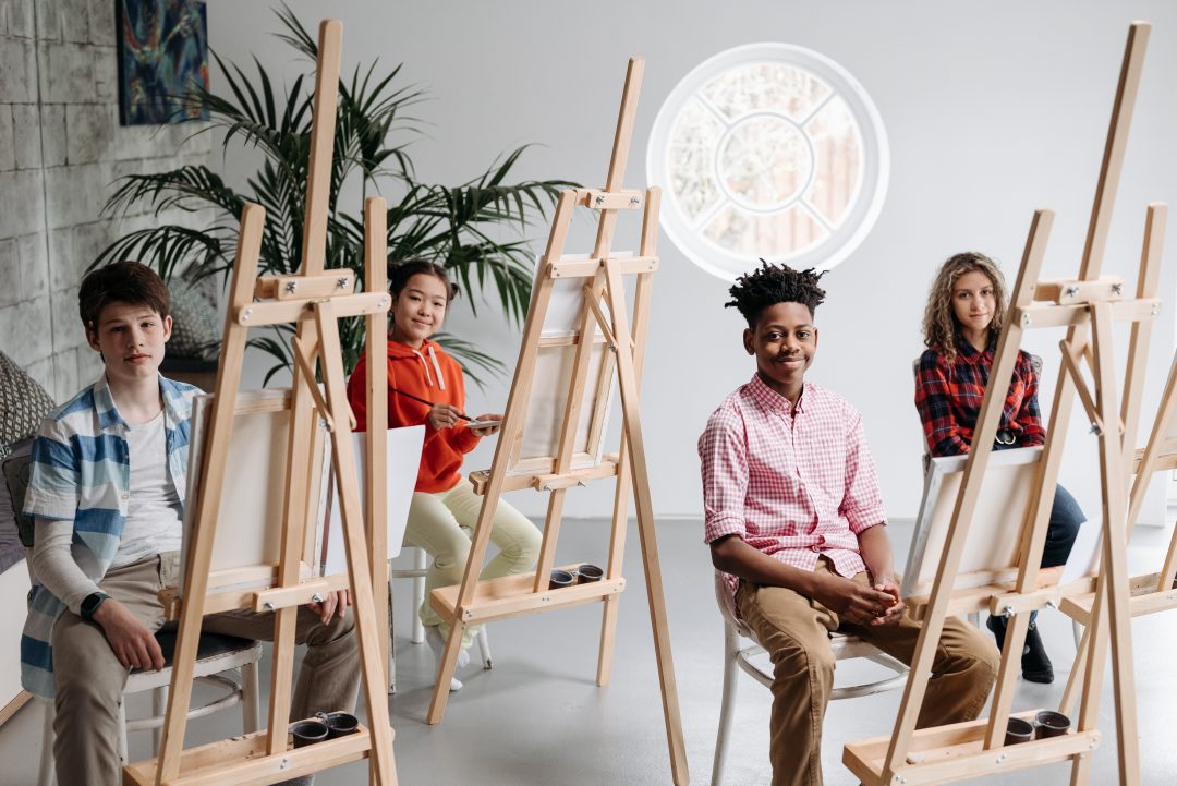 A diverse group of four students. Each is sitting in front of an easel.