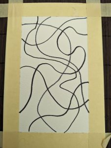 A piece of white paper is taped to a table. The paper has intersecting black wavy lines drawn with marker.