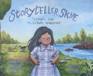The illustrated cover of a picture book is shown with the title in large blue font "Storyteller Skye" and in smaller black font, "Teachers from my Ojibway Grandfather". There is a smiling young girl with dark hair in a plaid violet and white dress and her hands on her hips. Behind her is a field and a river with trees in the background. There is a beaver in the water and in the field are a wolf chasing a dog and two white rabbits but one rabbit has very small ears. The author's name is Lindsay Christina King and the illustrator is Carolyn Frank.
