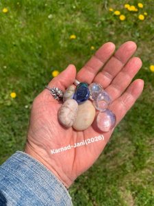 Three natural and 3 glass pebbles in the open palm of a left hand. The person is wearing a silver ring in the shape of a lotus. 